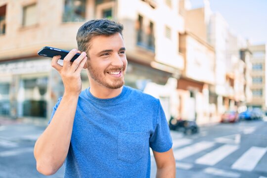 Young caucasian man smiling happy listening audio message using smartphone at the city.