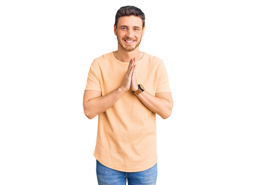 Handsome young man with bear wearing casual yellow tshirt praying with hands together asking for forgiveness smiling confident.