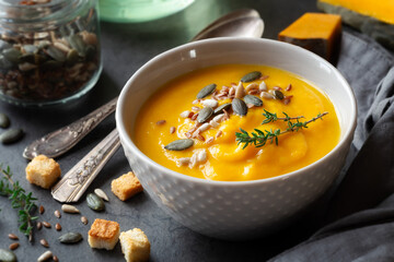 Pumpkin cream soup in a bowl garnished with mixed seeds and fresh thyme against dark rustic background