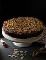 A cocoa cake filled with fruit jam and covered with chopped hazelnuts on a white stand and black background