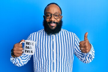 Young african american man drinking mug of coffe with best dad ever message smiling happy and positive, thumb up doing excellent and approval sign