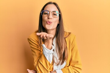 Young beautiful woman wearing business style and glasses looking at the camera blowing a kiss with hand on air being lovely and sexy. love expression.