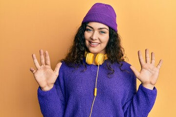 Young brunette woman with curly hair listening to music using headphones showing and pointing up...
