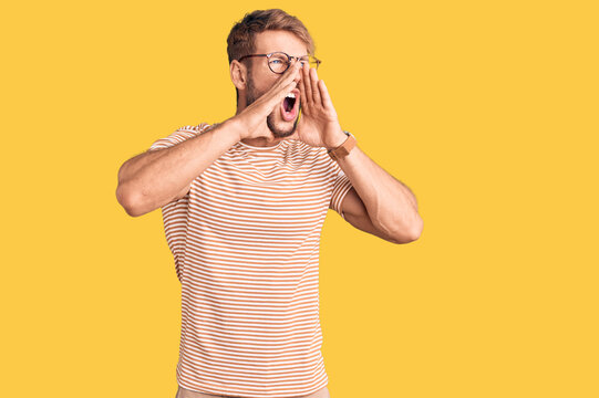 Young caucasian man wearing casual clothes and glasses shouting angry out loud with hands over mouth
