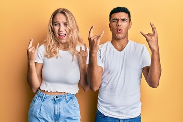 Young interracial couple wearing casual white tshirt shouting with crazy expression doing rock symbol with hands up. music star. heavy concept.