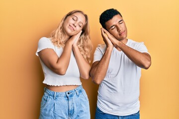 Young interracial couple wearing casual white tshirt sleeping tired dreaming and posing with hands together while smiling with closed eyes.