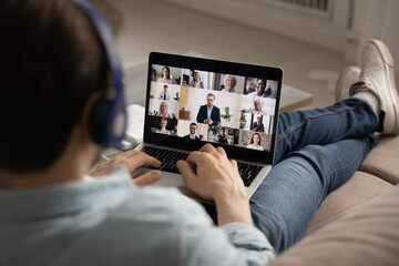 Rear view close up man wearing headphones engaged in online conference, group video call, using...