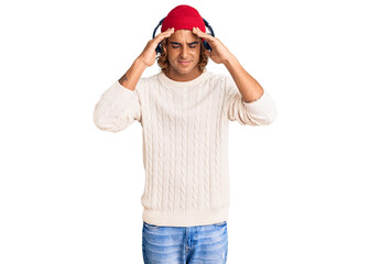 Young hispanic man listening to music using headphones with hand on head for pain in head because stress. suffering migraine.