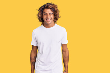 Young hispanic man wearing casual white tshirt winking looking at the camera with sexy expression,...