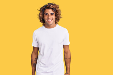 Young hispanic man wearing casual white tshirt winking looking at the camera with sexy expression, cheerful and happy face.