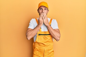 Young handsome man wearing handyman uniform over yellow background laughing and embarrassed giggle...
