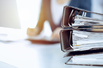 Binders with papers are waiting to be processed by business woman or bookkeeper working at the desk...