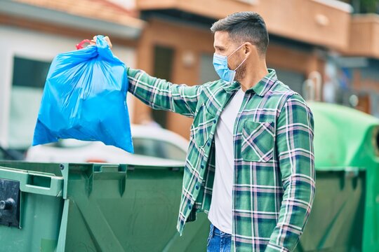 Young caucasian man wearing medical mask throwing waste bag to the container at the city.
