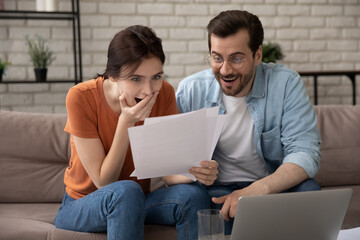 Overjoyed young couple reading letter together, happy surprised man and woman excited by received...