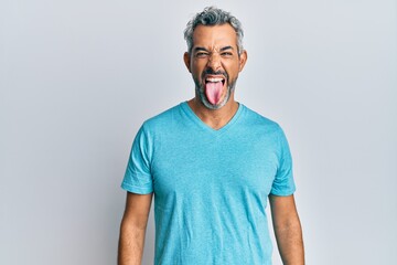 Middle age grey-haired man wearing casual clothes sticking tongue out happy with funny expression....