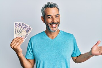 Middle age grey-haired man holding japanese yen banknotes celebrating achievement with happy smile and winner expression with raised hand