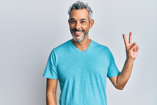 Middle age grey-haired man wearing casual clothes smiling with happy face winking at the camera doing victory sign. number two.