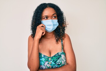 Young african american woman wearing medical mask thinking concentrated about doubt with finger on...