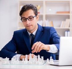 Young businessman playing glass chess in office