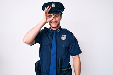 Young caucasian man wearing police uniform doing ok gesture with hand smiling, eye looking through fingers with happy face.