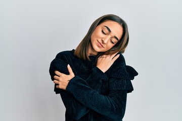 Young brunette girl wearing elegant fashion sweater hugging oneself happy and positive, smiling confident. self love and self care