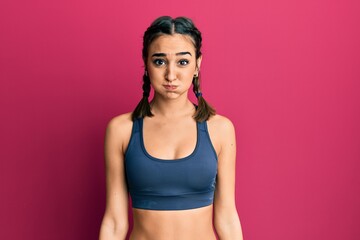 Fototapeta premium Young brunette girl wearing sportswear and braids puffing cheeks with funny face. mouth inflated with air, crazy expression.