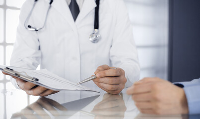 Unknown male doctor and woman-patient discussing current health examination while sitting in clinic...