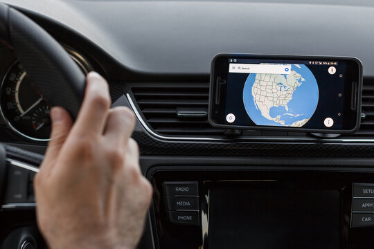 LOS ANGELES, CALIFORNIA - JUNE 6, 2019: Close up to male driving and using navigation application on the smartphone screen. Choose direction, globe on the screen. An illustrative editorial image