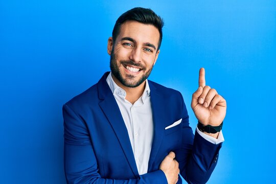 Young hispanic businessman wearing business jacket with a big smile on face, pointing with hand and finger to the side looking at the camera.