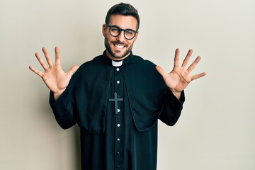 Young hispanic man wearing priest uniform standing over white background showing and pointing up...
