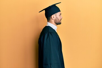 Young hispanic man wearing graduation cap and ceremony robe looking to side, relax profile pose...