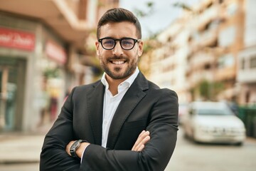 Fototapeta premium Young hispanic businessman with arms crossed smiling happy at the city.