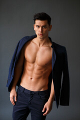 Elegant, muscular, handsome brunette man sitting and posing in fashionable suit on a naked torso,...