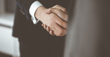 Obraz premium Unknown businessman shaking hands with his colleague or partner while standing straight in modern office, close-up. Business people group at meeting