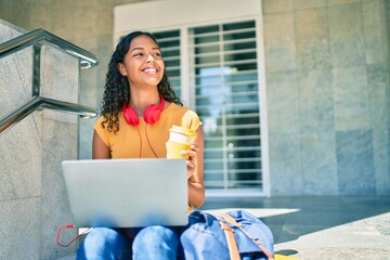 Young african american student girl using laptop sitting on stairs at university.