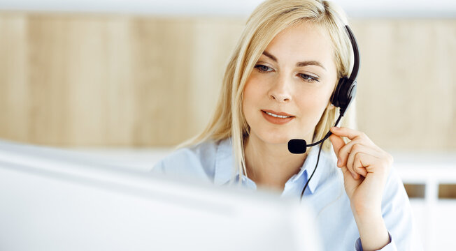 Blonde business woman sitting and communicated by headset in call center office. Concept of telesales business or home office occupation