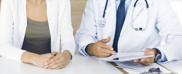 Doctor and patient discussing medical exam results while sitting at the desk in clinic, close-up....