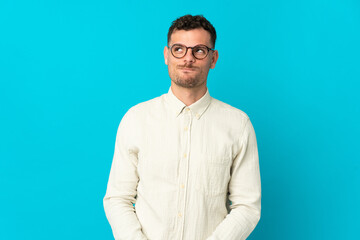 Young caucasian handsome man isolated on blue background having doubts while looking up