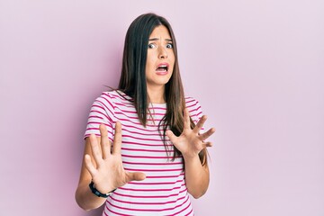 Young brunette woman wearing casual clothes over pink background afraid and terrified with fear expression stop gesture with hands, shouting in shock. panic concept.