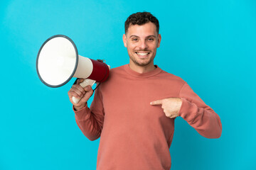 Young caucasian handsome man isolated on blue background holding a megaphone and with surprise...