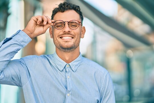 Young hispanic businessman smiling happy touching his glasses at the city.