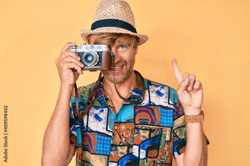 Poster young blond man using vintage camera smiling with an idea or question pointing finger with happy fac