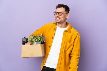 Young caucasian man making a move while picking up a box full of things isolated on purple...