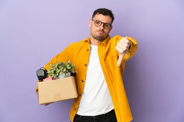 Young caucasian man making a move while picking up a box full of things isolated on purple...