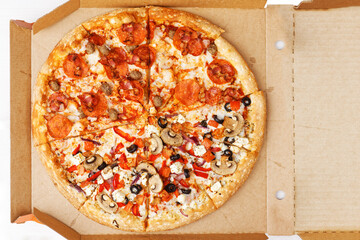 Half meat and half vegetable pizza in open cardboard box. Top view.