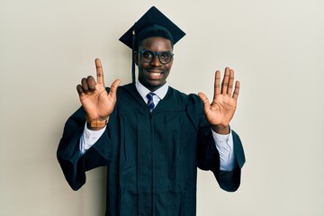 Handsome black man wearing graduation cap and ceremony robe showing and pointing up with fingers...