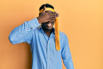 Handsome black man drunk wearing tie over head and sunglasses smiling and laughing with hand on face covering eyes for surprise. blind concept.