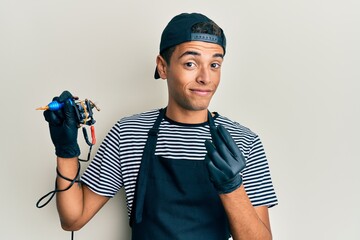 Young handsome african american man tattoo artist wearing professional uniform and gloves holding tattooer machine doing money gesture with hands, asking for salary payment, millionaire business