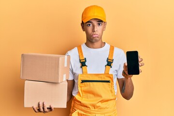 Young handsome african american man holding delivery package and showing smartphone screen depressed and worry for distress, crying angry and afraid. sad expression.