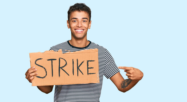 Young handsome african american man holding strike banner cardboard smiling happy pointing with hand and finger